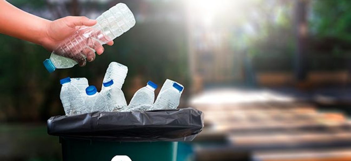reciclagem na Ecoassist: conceito, importância e curiosidades. Na imagem, mão de uma pessoa jogando uma garrafa plástica dentro de uma lixeira verde com símbolo de reciclagem.